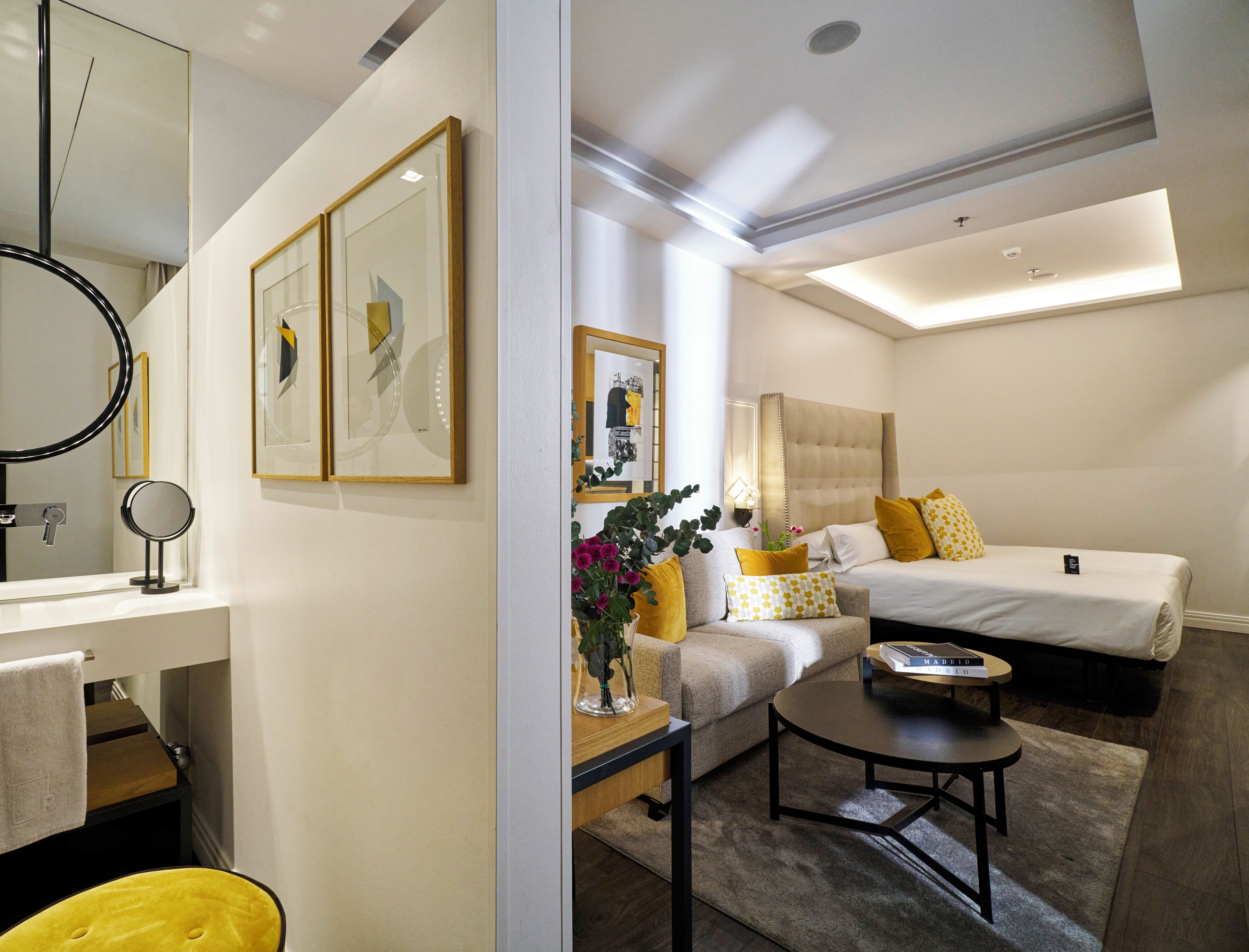 Ein modernes Hotelzimmer mit einem Bett, einer Couch, einem Couchtisch, einem kleinen Tisch mit einer Lampe und einem Spiegel.