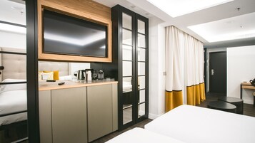 Ein modernes Hotelzimmer mit einem Bett, einem Schreibtisch mit Kaffeemaschine und einem an einer Holzplatte montierten Fernseher.