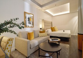 A modern hotel room with a sofa, a bed, a round coffee table, and a large mirror.