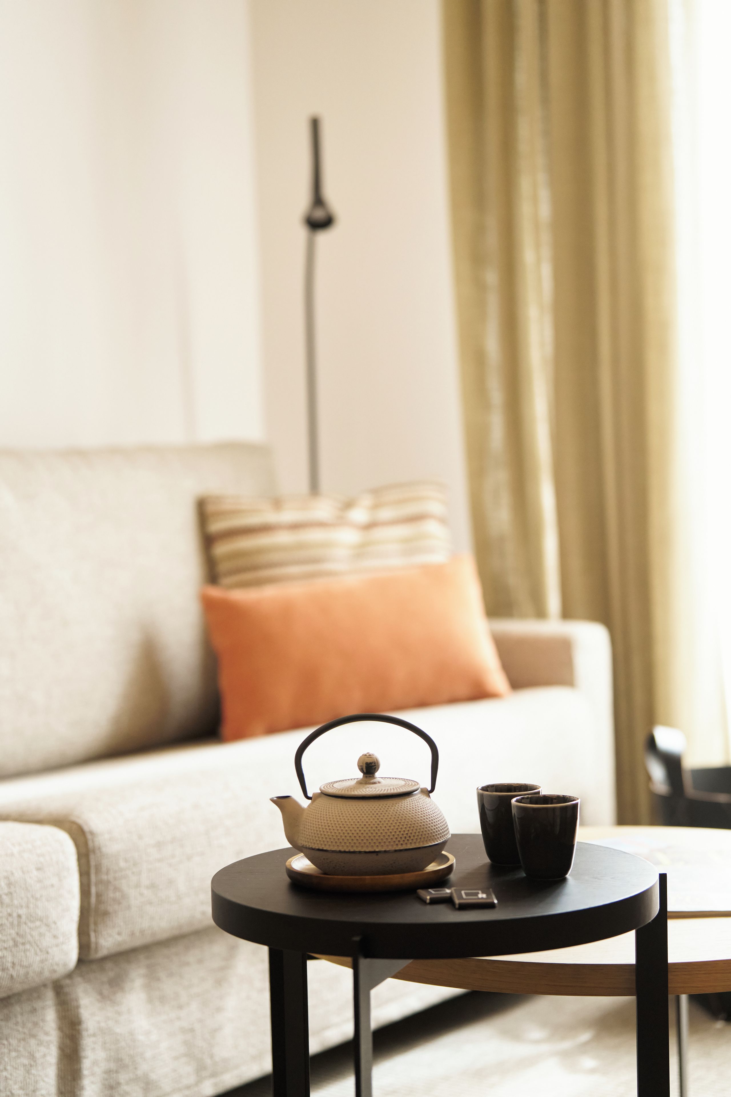 Ein gemütliches Wohnzimmer mit einer Couch, einem kleinen runden Tisch mit Teekanne und Tassen sowie einer Lampe im Hintergrund.