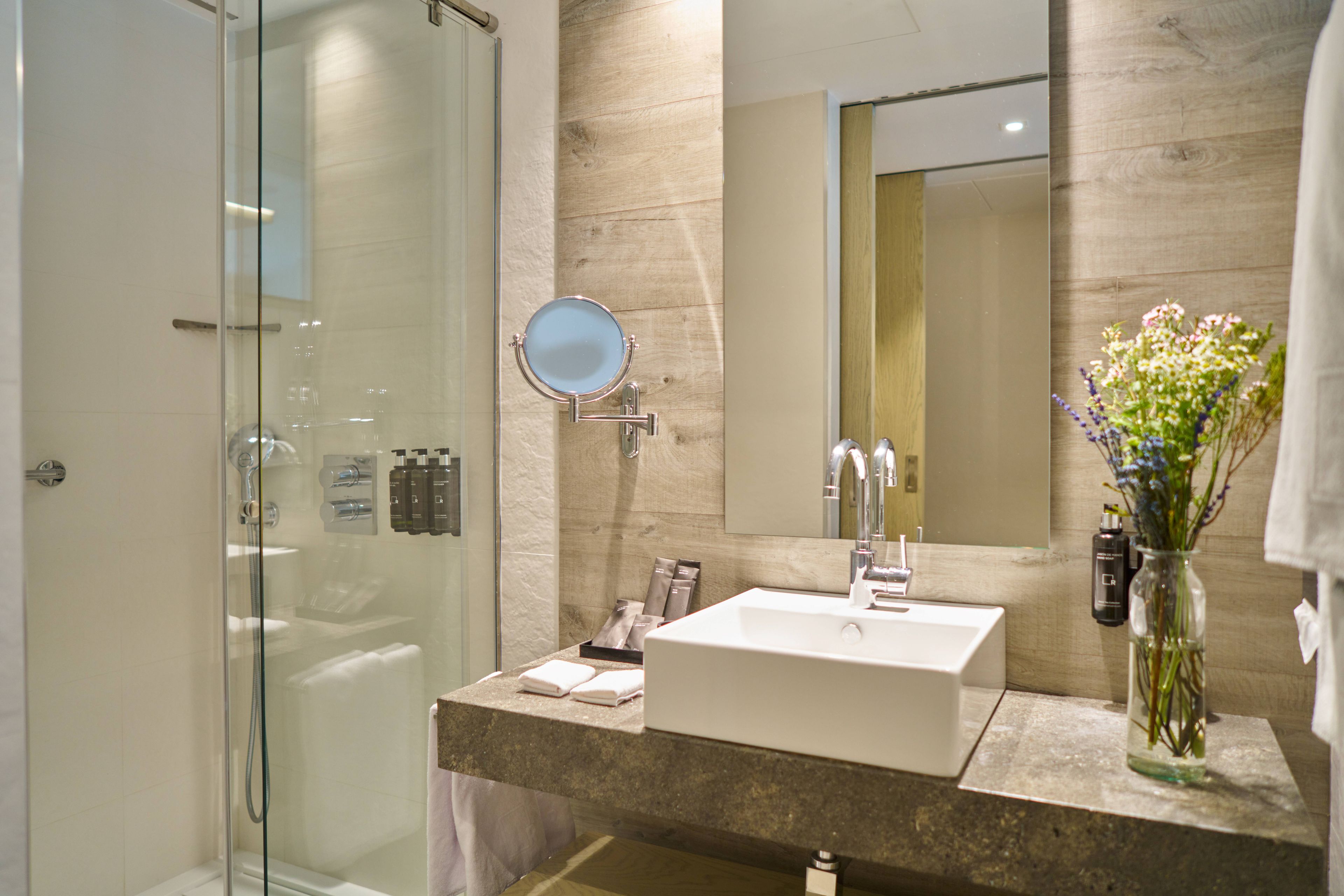 A modern bathroom with a glass shower enclosure, a white sink, and a mirror.