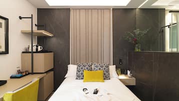 Una habitación de hotel moderna con una cama, una mesita de noche, un escritorio y un espejo.
