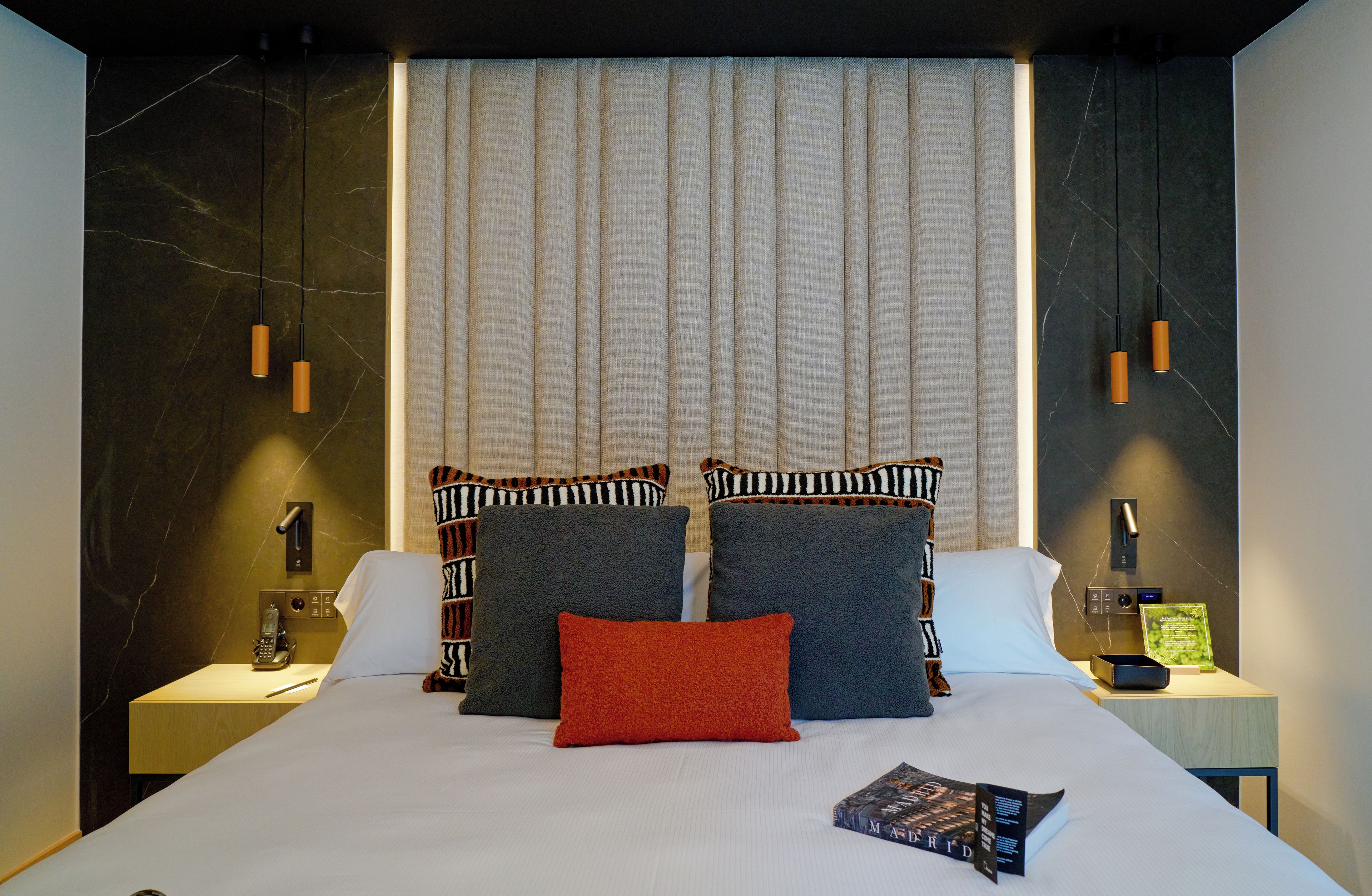 A modern hotel room with a large bed, two bedside tables, a telephone, and a book on the bed.
