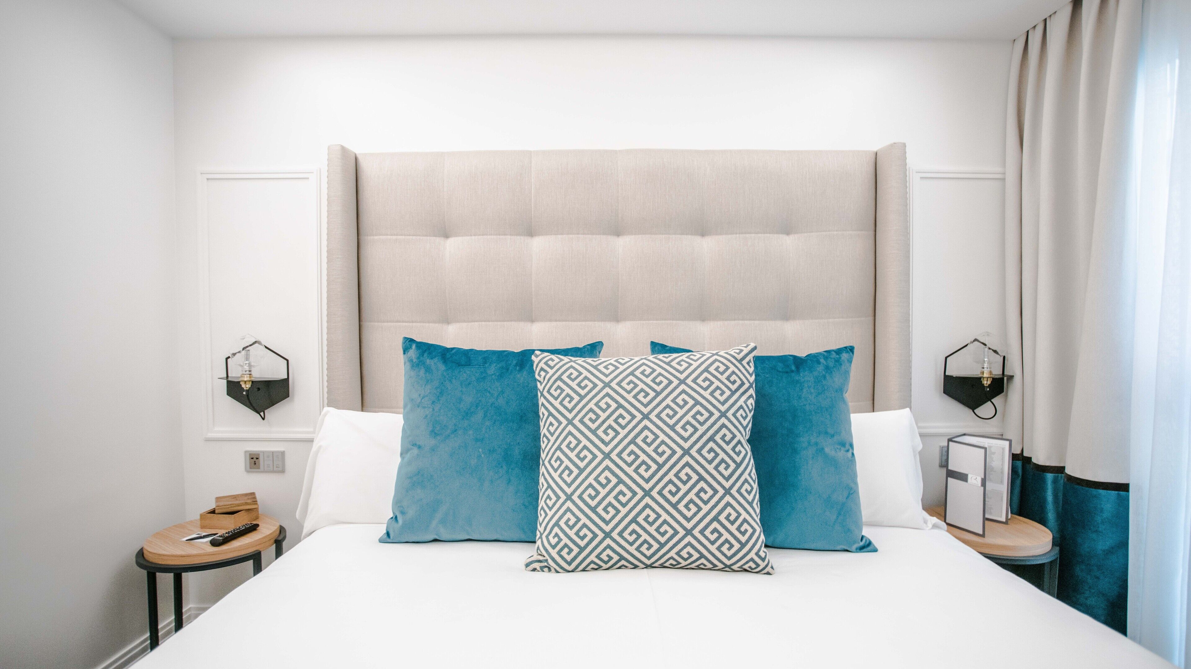 A neatly made bed with a tufted headboard, two bedside tables with lamps, and a nightstand with a remote control.