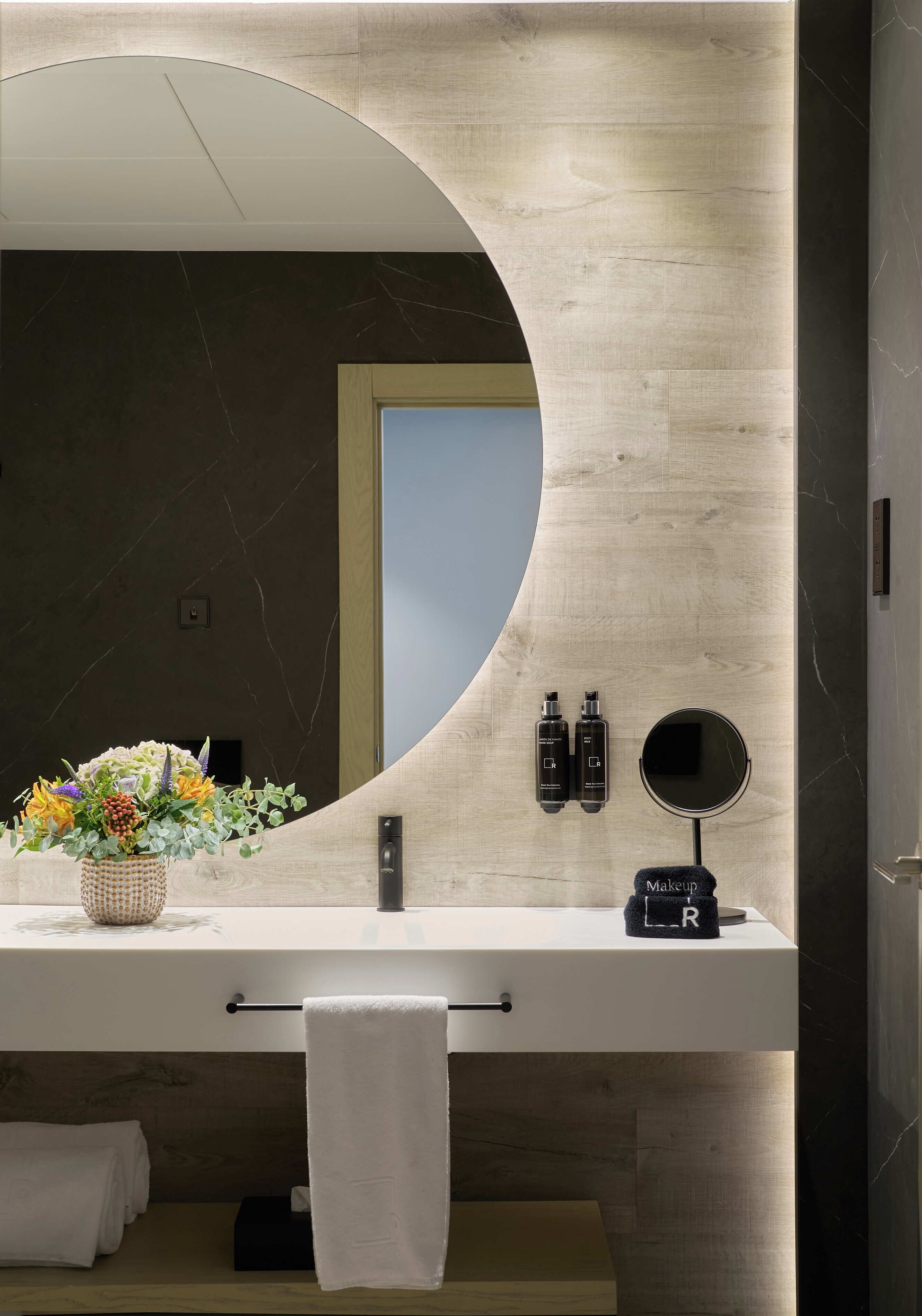 Ein modernes Badezimmer mit einem großen Spiegel, einem Handtuchhalter, einem Waschbecken und einer Blumenvase.