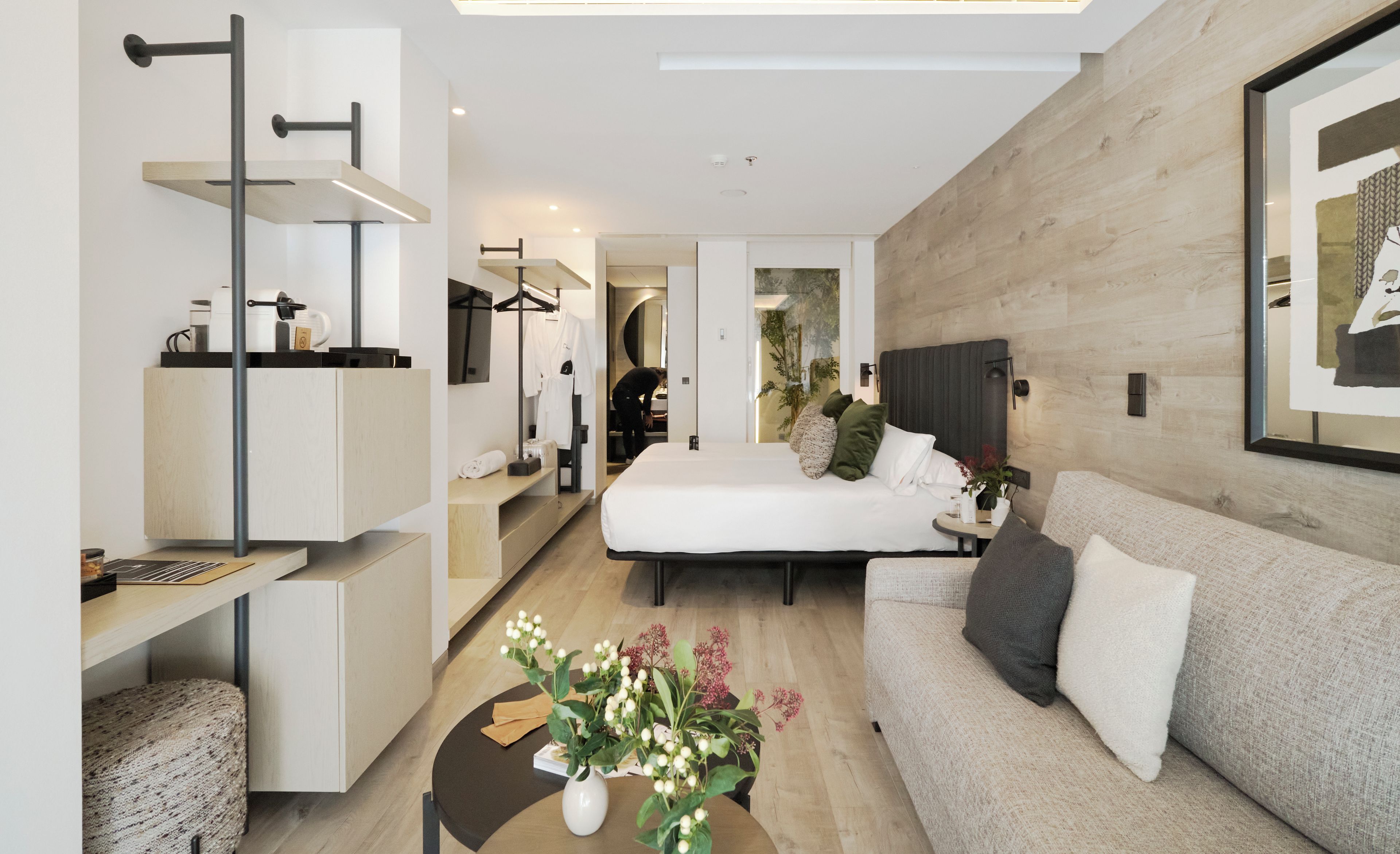 A modern hotel room with a bed, sofa, and a desk with a computer.