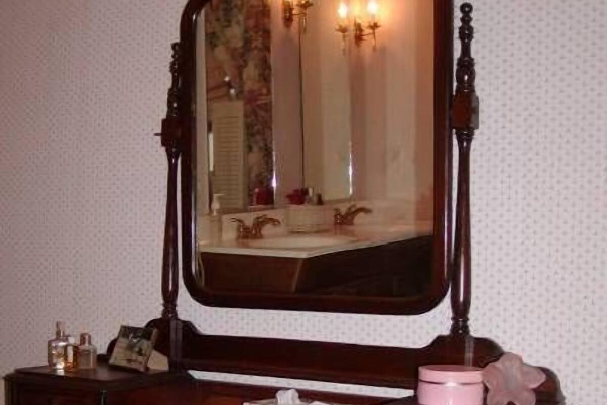 A wooden vanity with a large mirror, a small bench, and a few personal items.