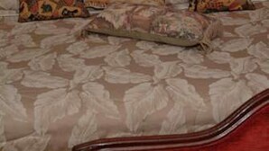 Une pièce avec un canapé à motifs floraux, trois coussins assortis et une tête de lit en bois.