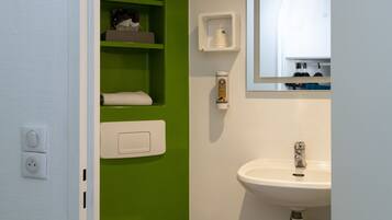 A bathroom with a white sink, green shelves, a toilet, and a mirror.