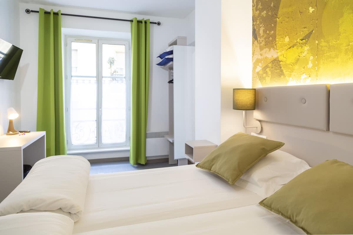 A hotel room with a bed, green curtains, a TV on the wall, and a lamp.