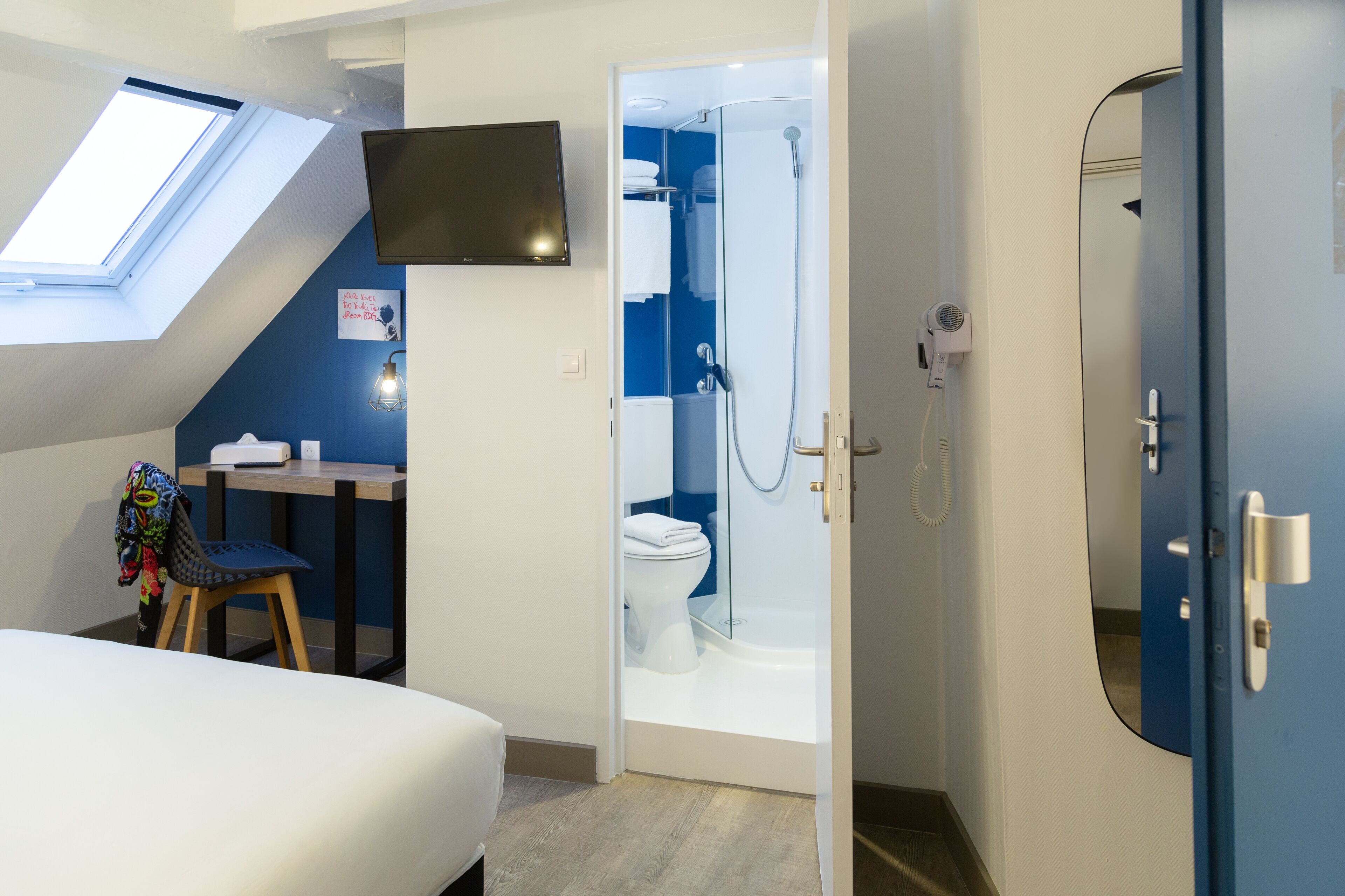 A bedroom with a skylight, a desk, a chair, and a bed.