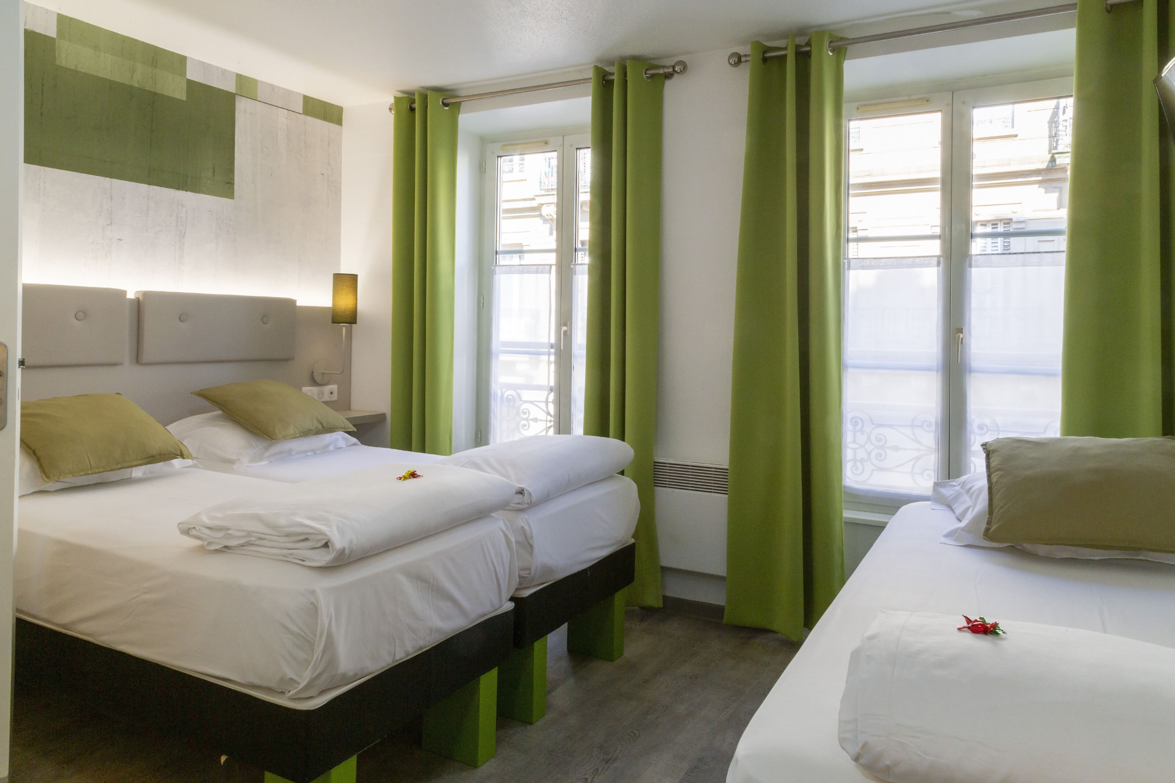 Ein Hotelzimmer mit zwei Betten, grünen Vorhängen und Blick auf die Stadt.