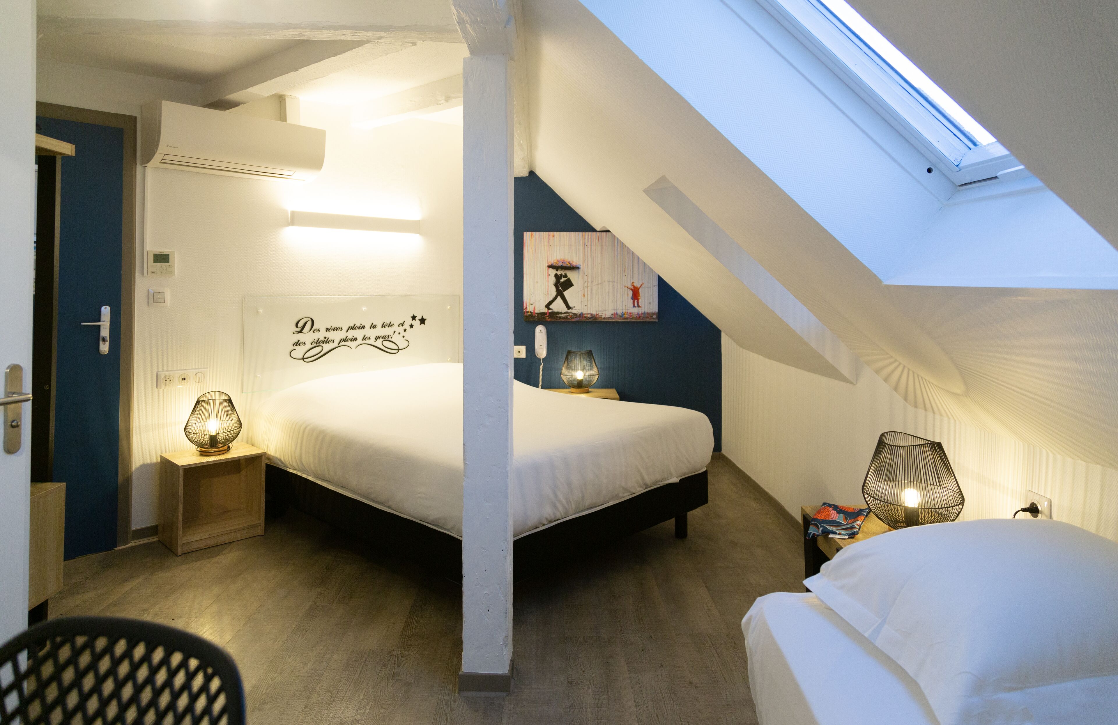 Un dormitorio con tragaluces, una cama, lámparas de noche y una pared con un letrero decorativo.