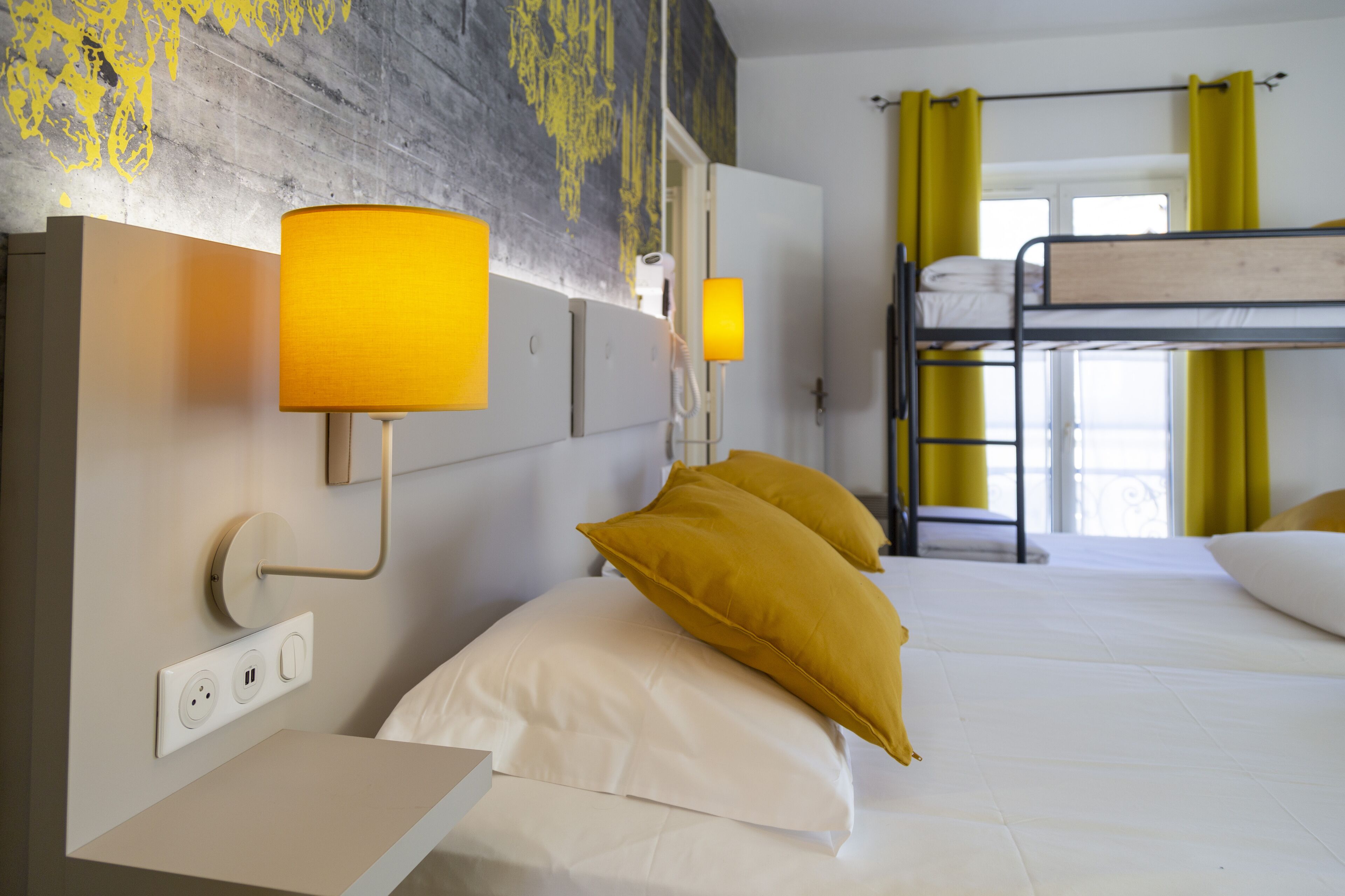 A hotel room with a bunk bed, a bedside table, and a wall-mounted lamp.