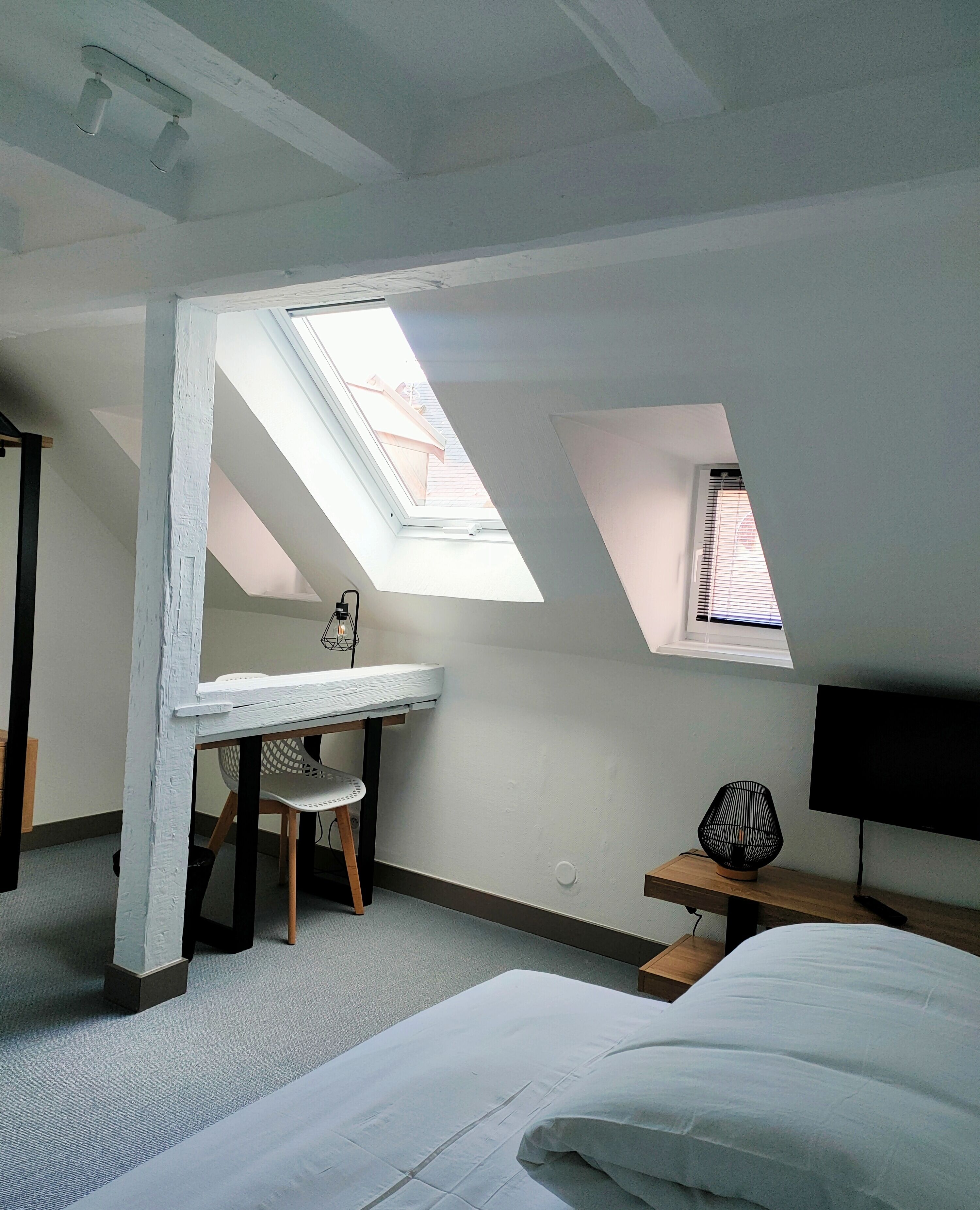 A bedroom with a skylight, a desk, a chair, a bed, and a TV.