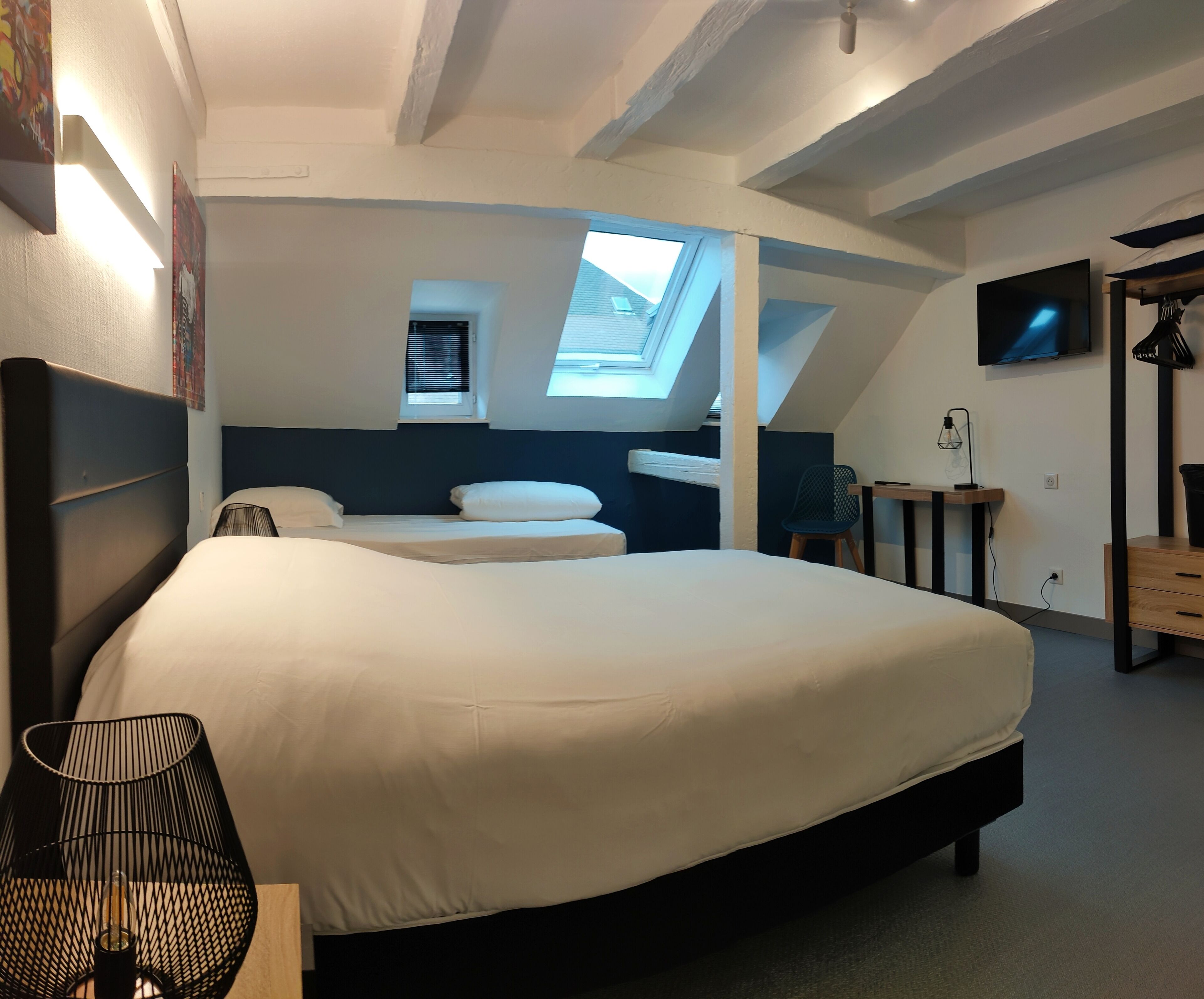Un dormitorio moderno con una cama grande, tragaluces y televisión en la pared.