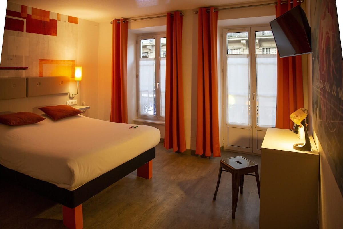 A hotel room with a bed, a desk, a chair, a TV, and a window with curtains.