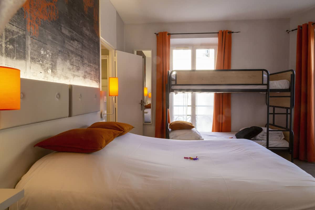 A hotel room with a bunk bed, a single bed, orange curtains, and a painting on the wall.