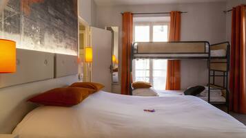 Une chambre d’hôtel avec un lit superposé, un lit simple, des rideaux orange et un tableau au mur.