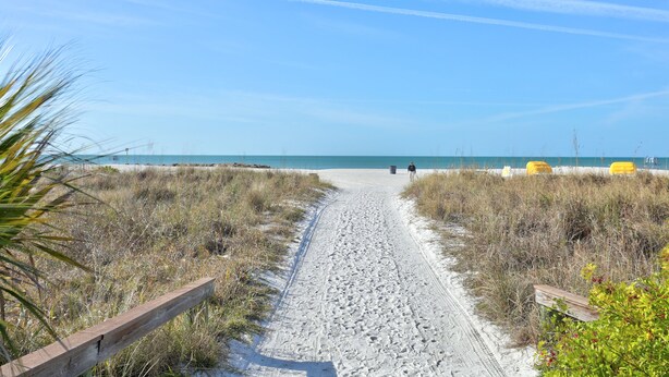 A sandy path leading to a beach with a wooden fence on one side and yellow chairs on the other. - Gulf Winds Beach Resort (St. Pete Beach)