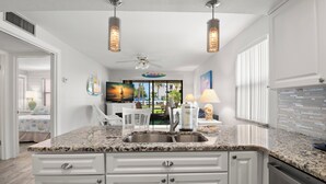 A kitchen with granite countertops, white cabinetry, and pendant lighting. - Gulf Winds Beach Resort (St. Pete Beach)