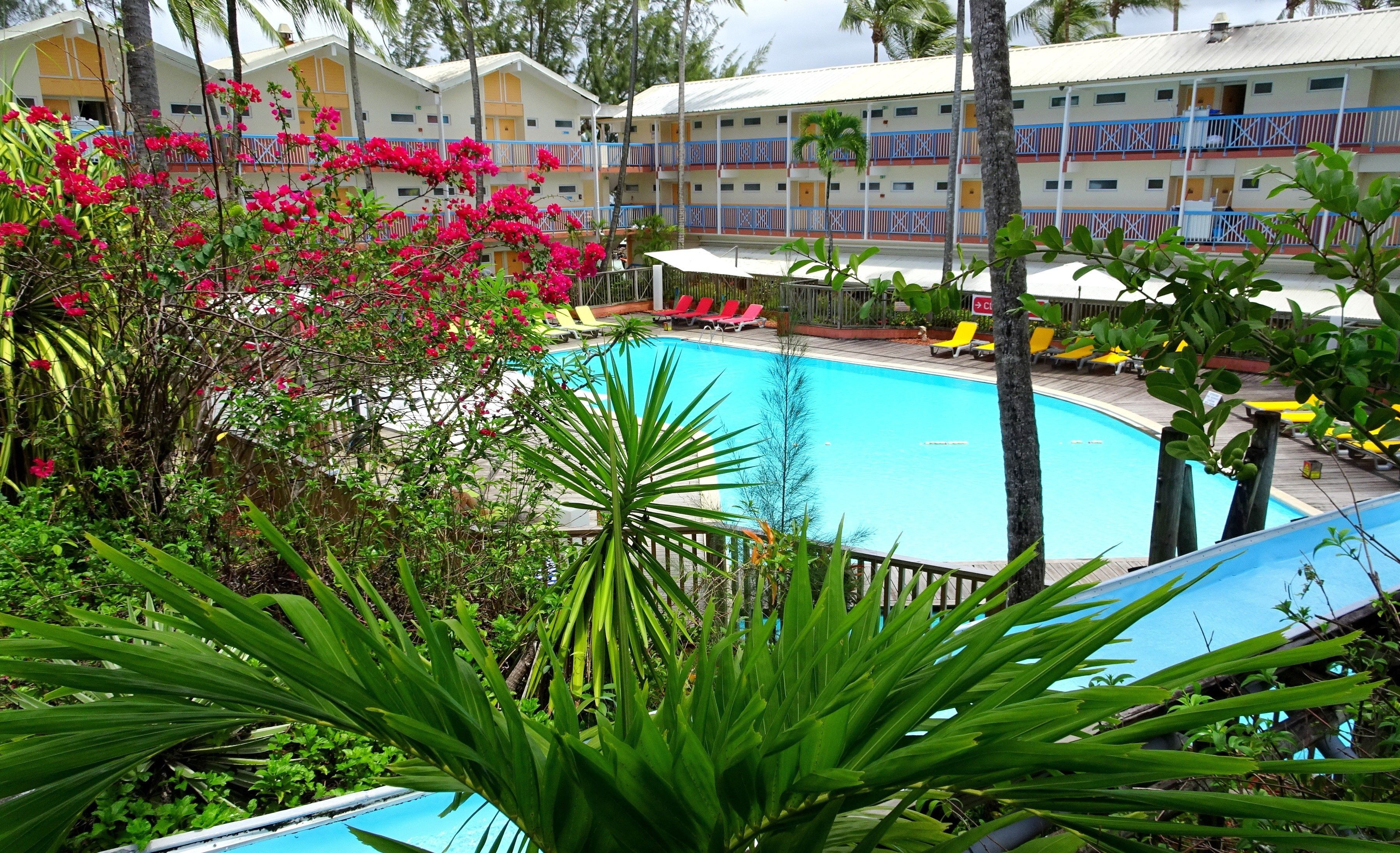 A hotel with a swimming pool surrounded by lush greenery and pink flowers.