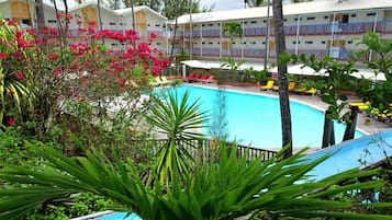 Un hotel con piscina rodeado de exuberante follaje y flores rosadas.