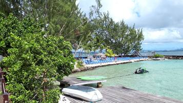 A beachside resort with a wooden deck, lounge chairs, and a small boat.