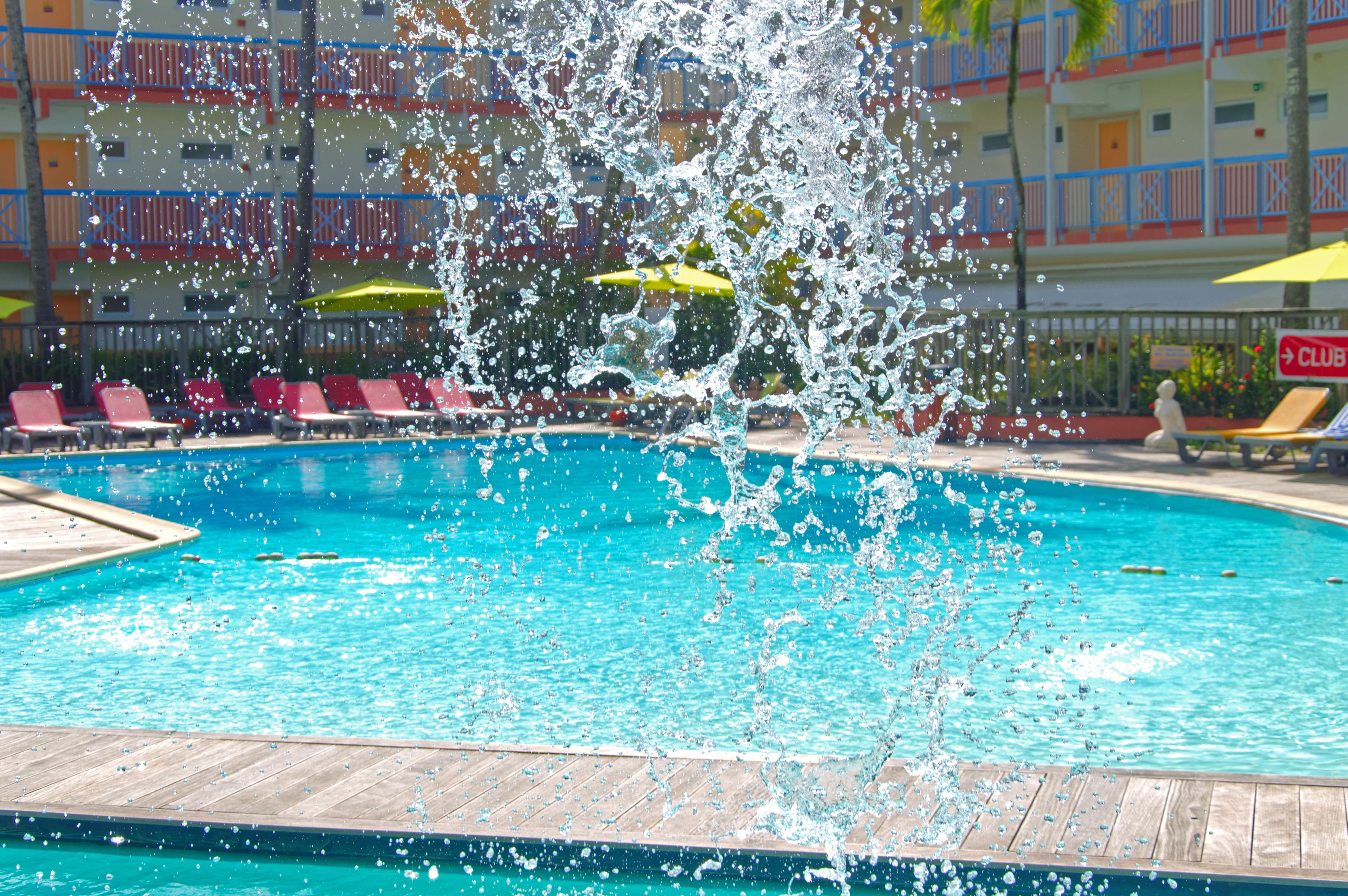 A swimming pool with water splashing, surrounded by lounge chairs and umbrellas.