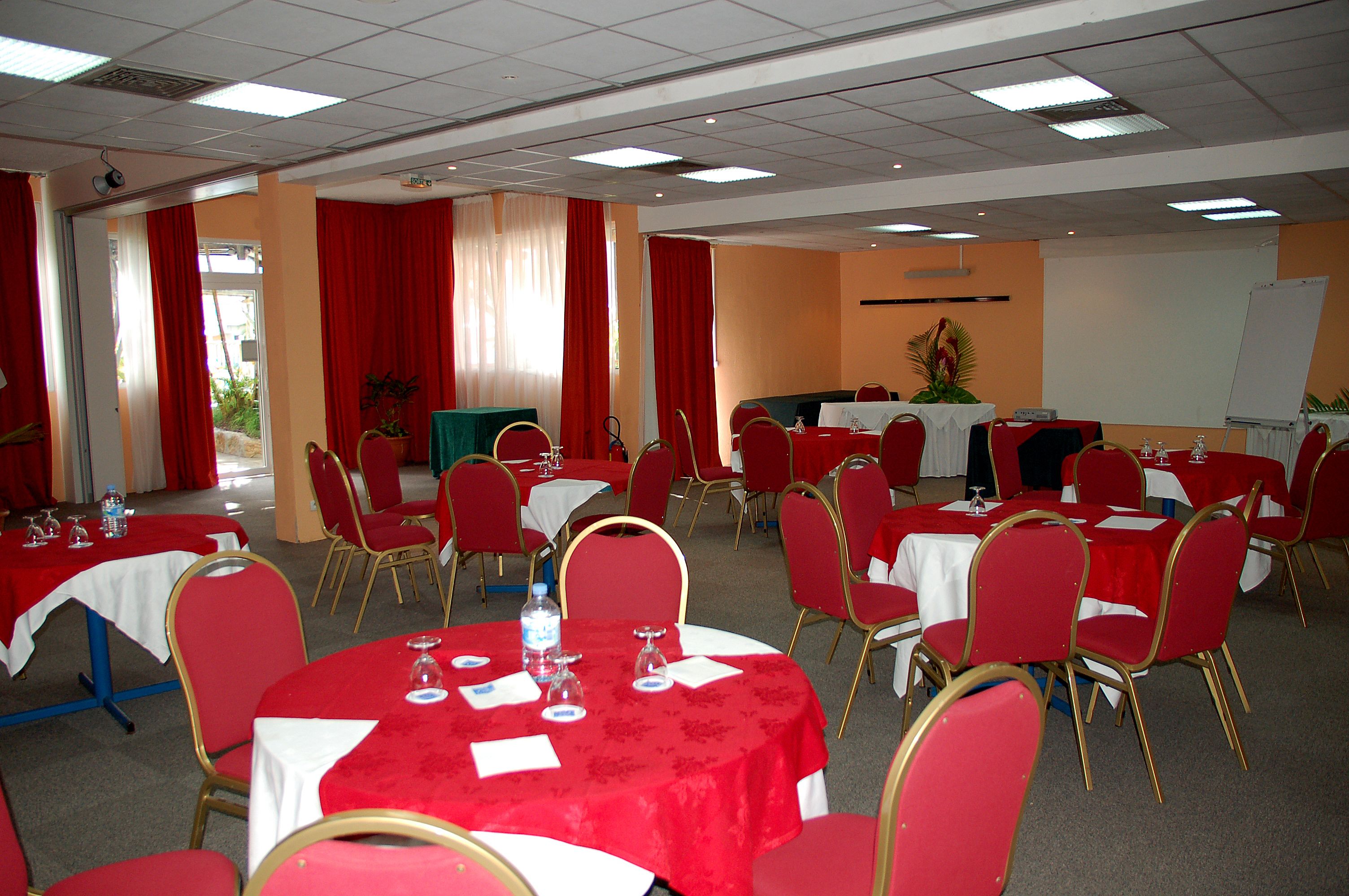 A conference room with multiple tables and chairs, red curtains, and a whiteboard.