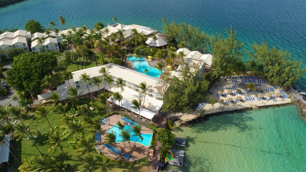 Luchtbeeld van een resort met meerdere zwembaden, strandgebieden en weelderige begroeiing.
