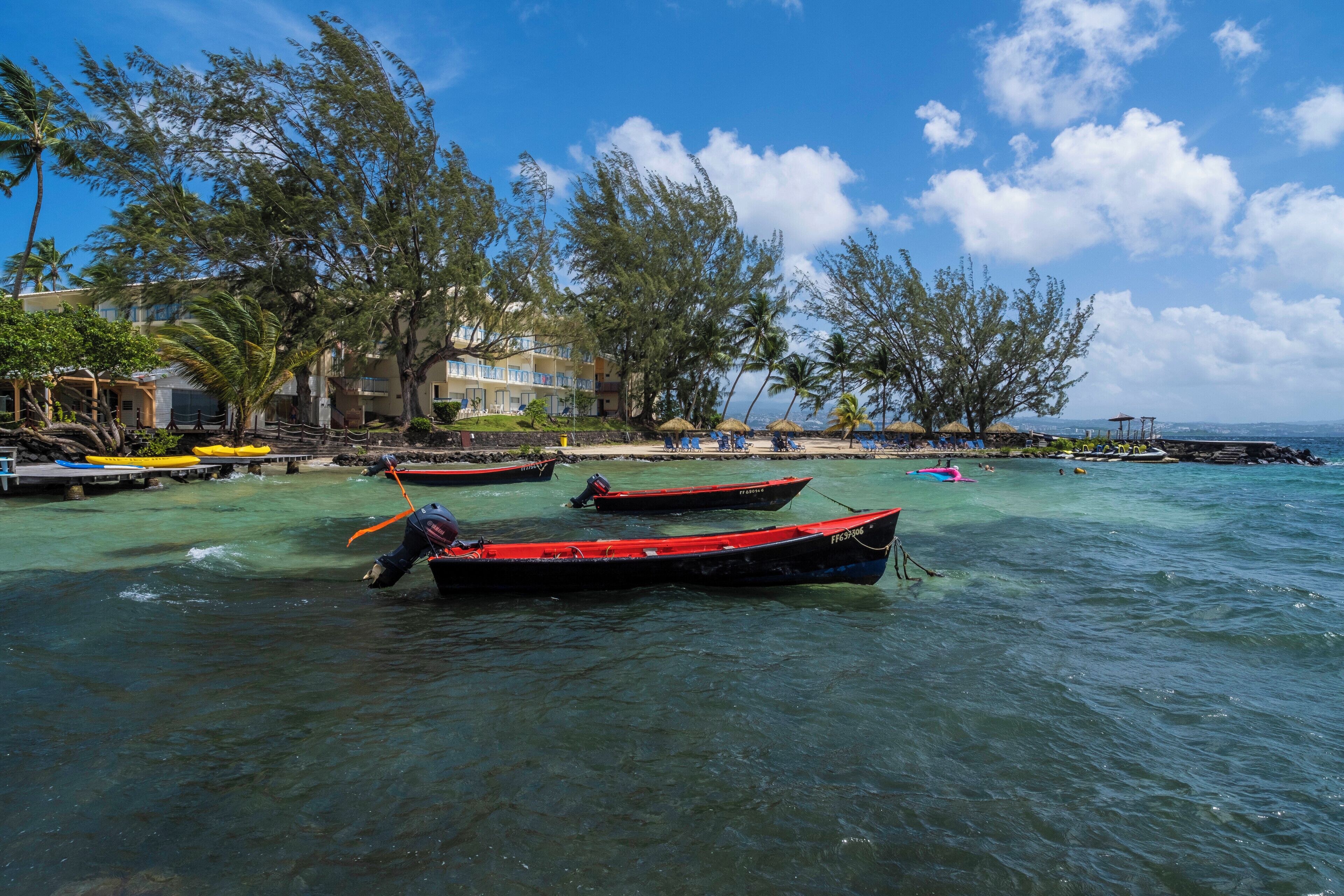 Una playa con aguas cristalinas, barcos y un edificio con balcones que dan al mar.
