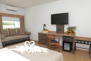 Una camera d'albergo con un letto, un divano, una scrivania con televisore, un piccolo frigorifero e una finestra con tende.