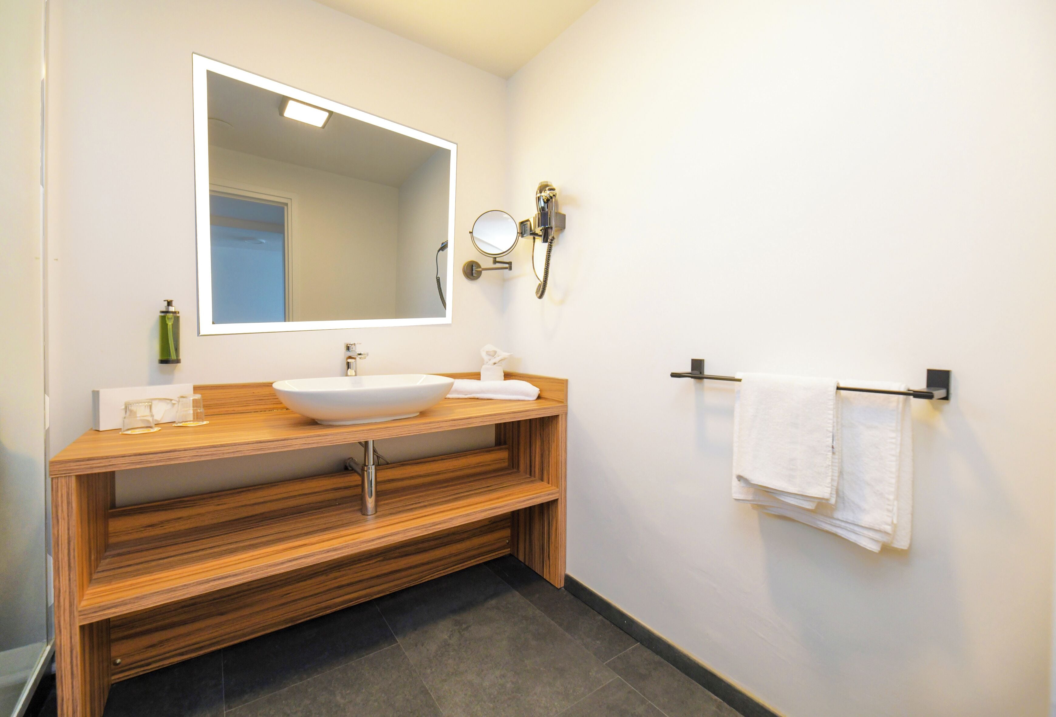 Une salle de bain moderne avec un meuble-lavabo en bois, un grand miroir, un lavabo, un porte-serviettes et une douchette à main.