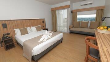 Una camera d'albergo con un letto, un divano, una scrivania con una sedia e vista sul mare.