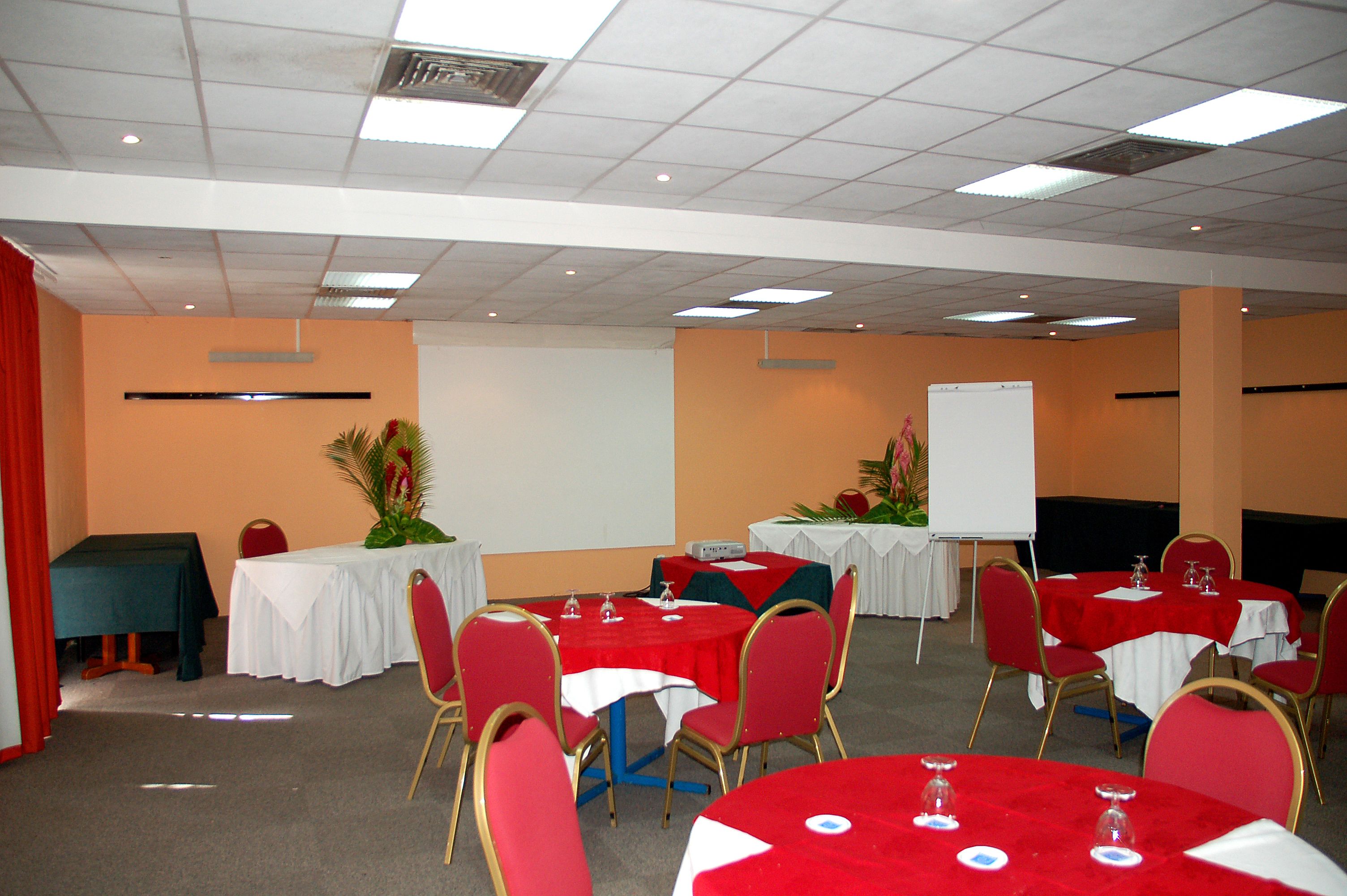 A conference room with multiple tables and chairs, whiteboard, and a projector screen.