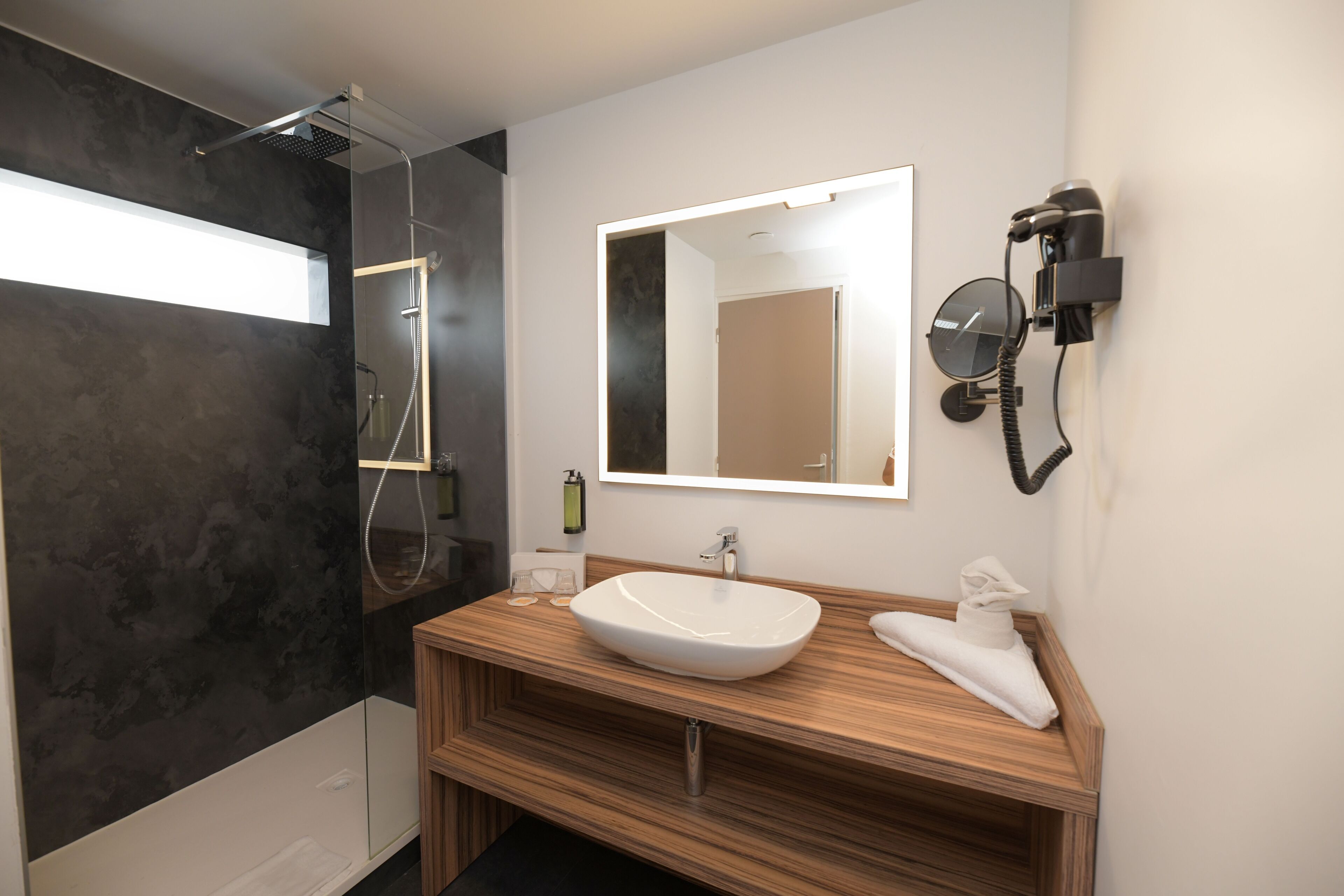 A modern bathroom with a wooden vanity, a large mirror, and a built-in shower.