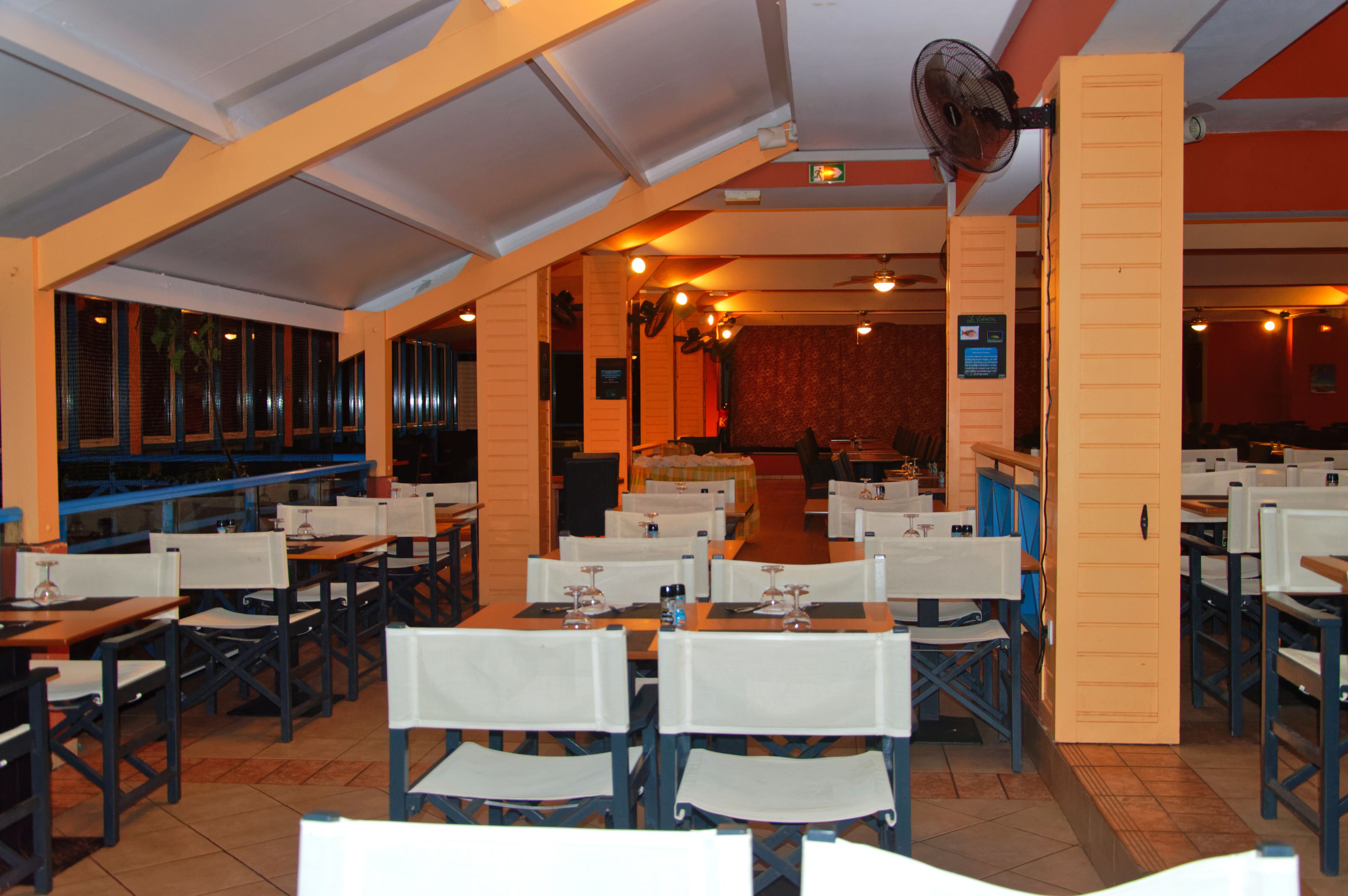 An indoor dining area with tables and chairs, a stage with curtains, and a fan on the ceiling.