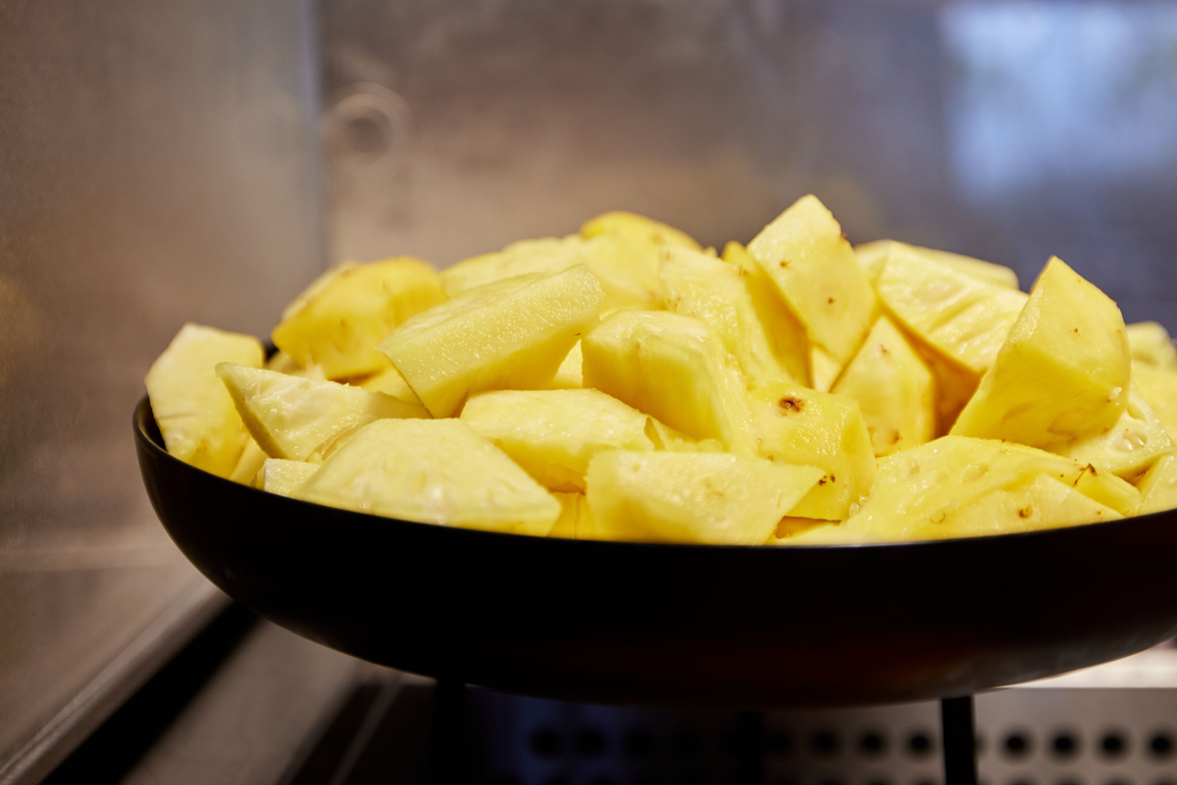 A bowl of diced yellow fruit, likely pineapple, on a stove.