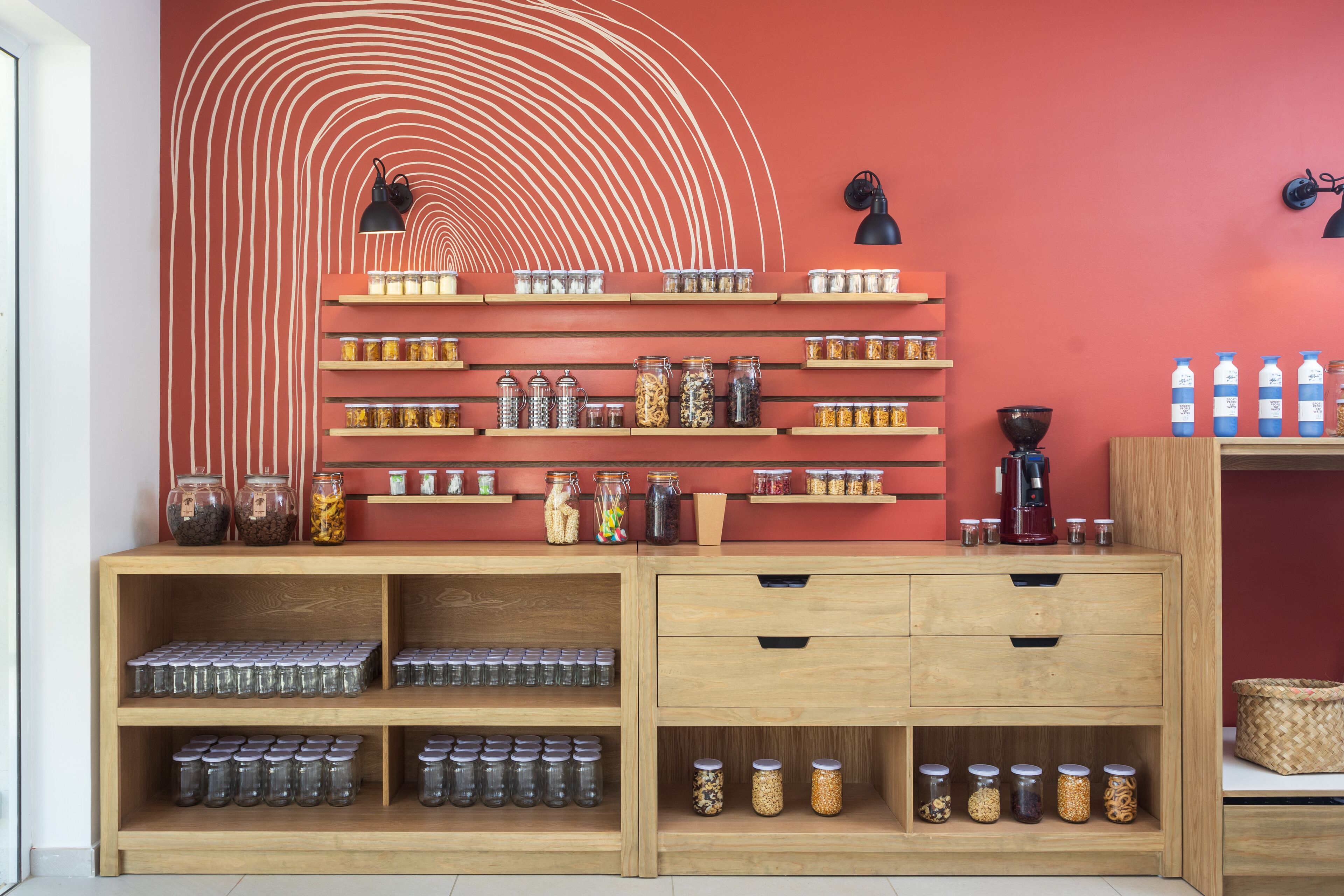 Une cuisine avec des meubles de rangement en bois, des étagères remplies de bocaux et un mur rouge orné d’un motif blanc.