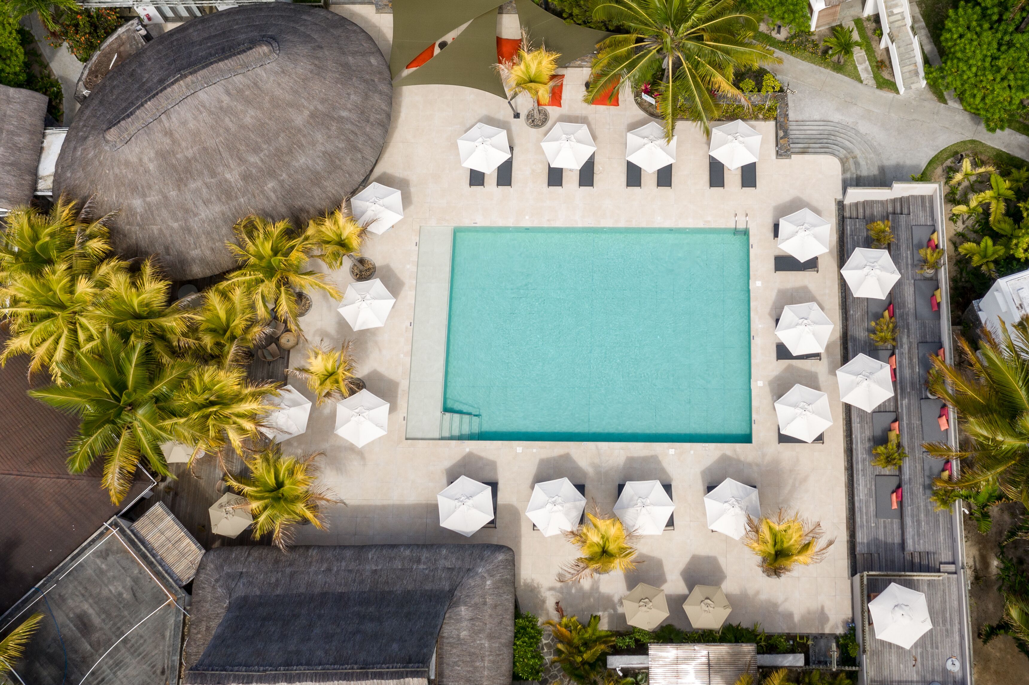 Luchtbeeld van een resort met een centraal gelegen zwembad, loungegedeeltes met parasols en palmbomen.