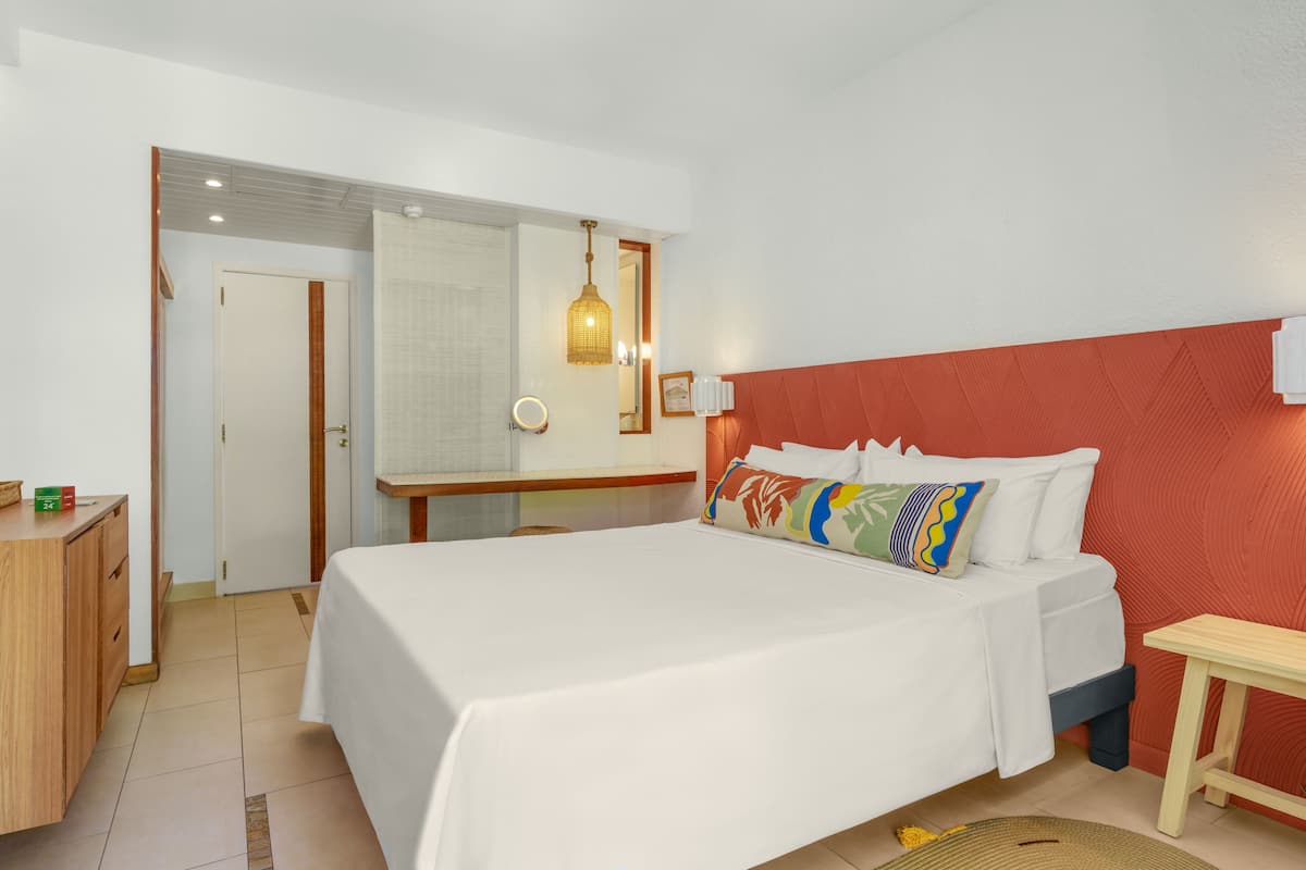 Habitación de hotel con una cama grande, un escritorio de madera, un espejo y una pared de acento roja.