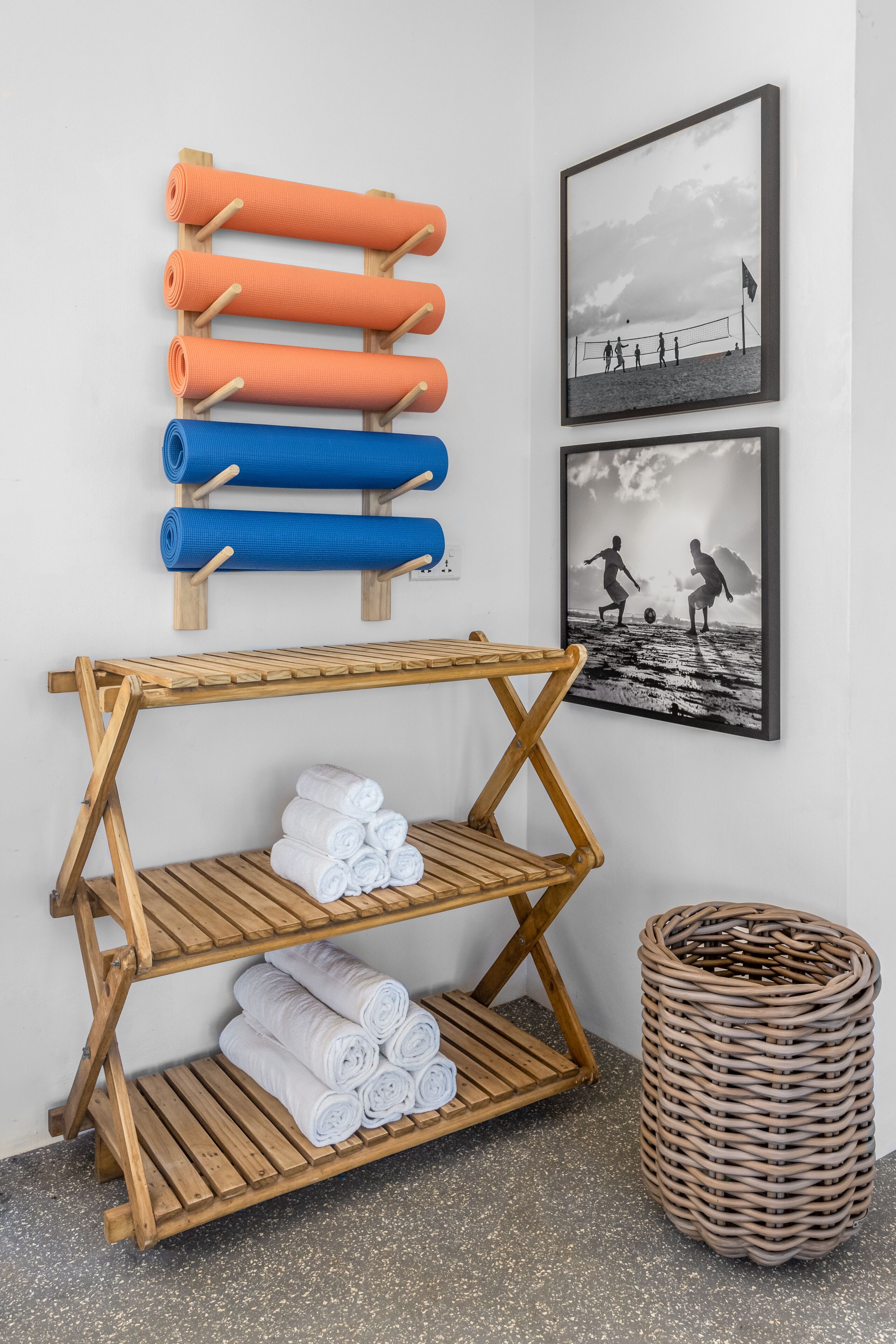 A wooden shelf with rolled towels in orange, blue, and white, and a wicker basket on the floor.