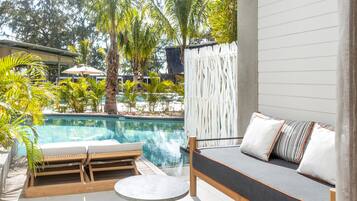 A poolside area with a wooden lounge chair, a small round table, and a sofa with cushions.