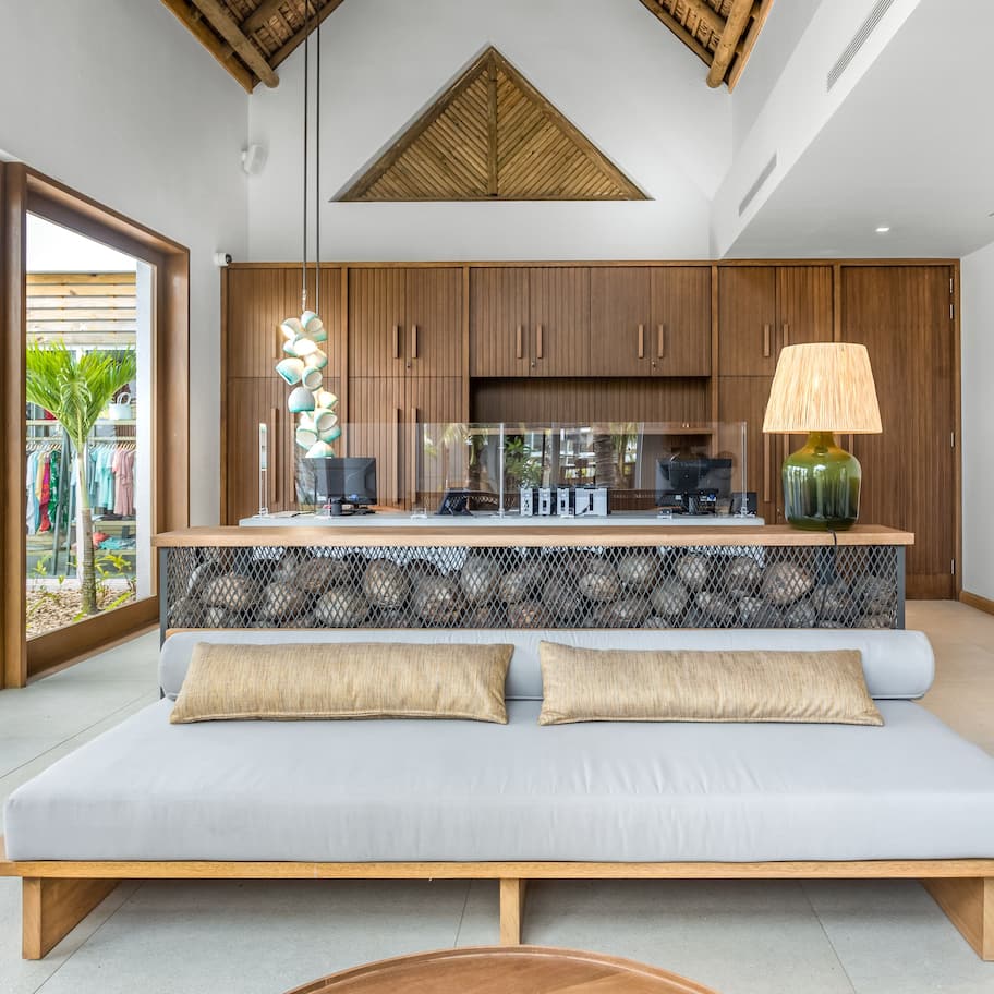 A modern living room with a sofa, a dining area with wooden cabinets, and a large window providing a view of the outdoors.