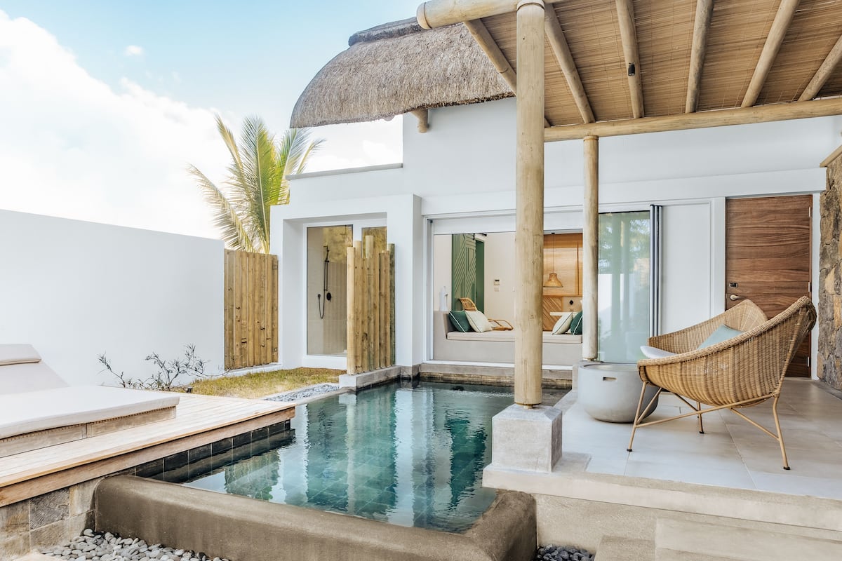 Un área de piscina moderna al aire libre con techo de paja, terraza de madera y silla de mimbre.
