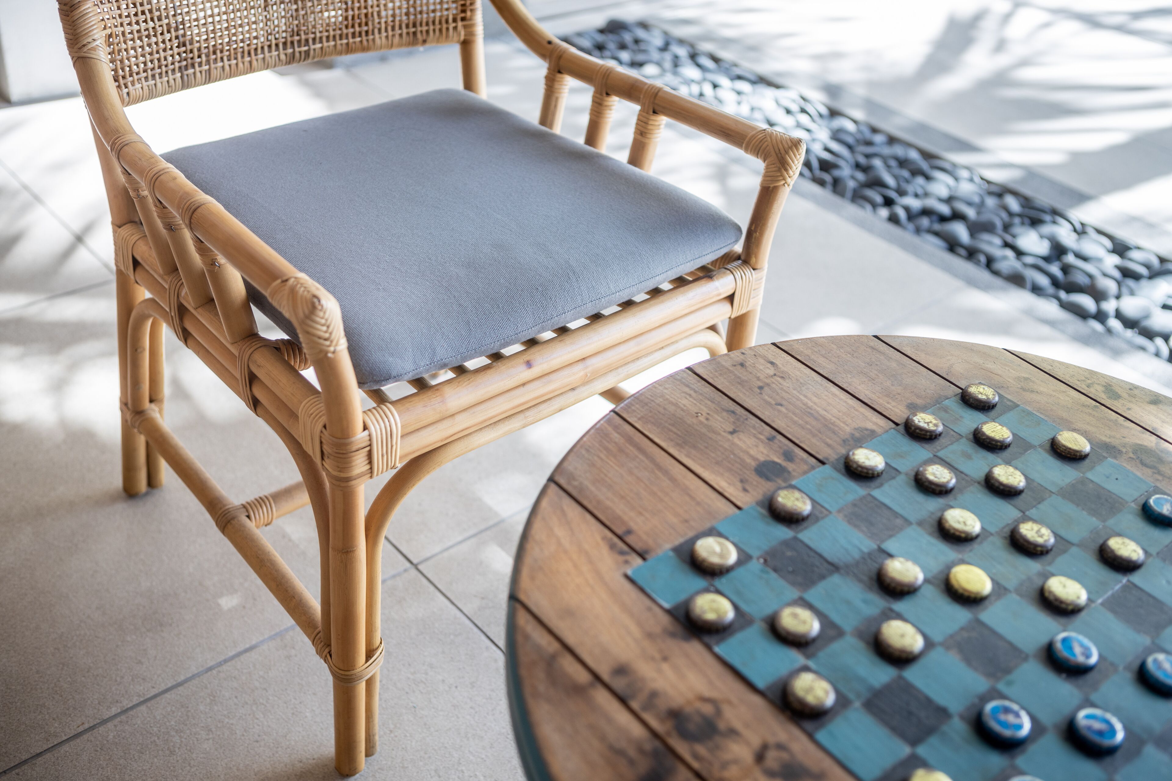 Una silla de mimbre con un cojín gris y una mesa redonda de madera con un juego de mesa de tablero.