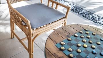 Una silla de mimbre con un cojín gris y una mesa redonda de madera con un juego de mesa de tablero.