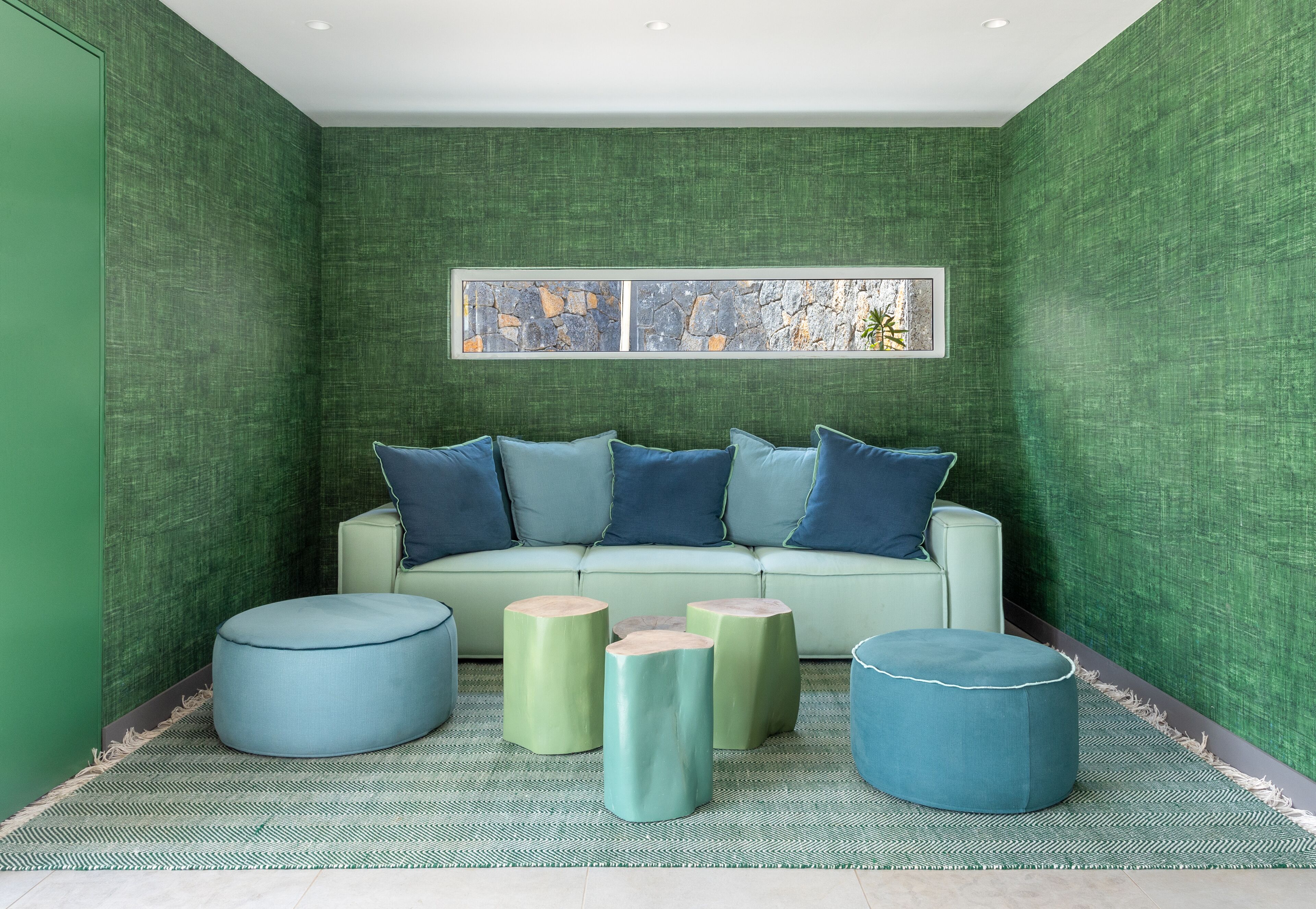 A green-walled room with a light green sofa, blue cushions, and matching ottomans.