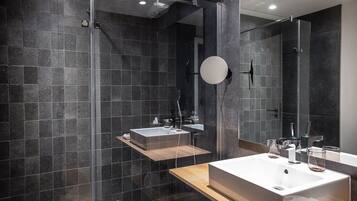 A modern bathroom with dark tiled walls, a glass shower enclosure, and two sinks with wooden countertops.